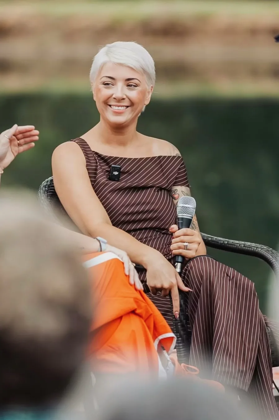 Jes Carlson smiling, holding a microphone while seated on stage